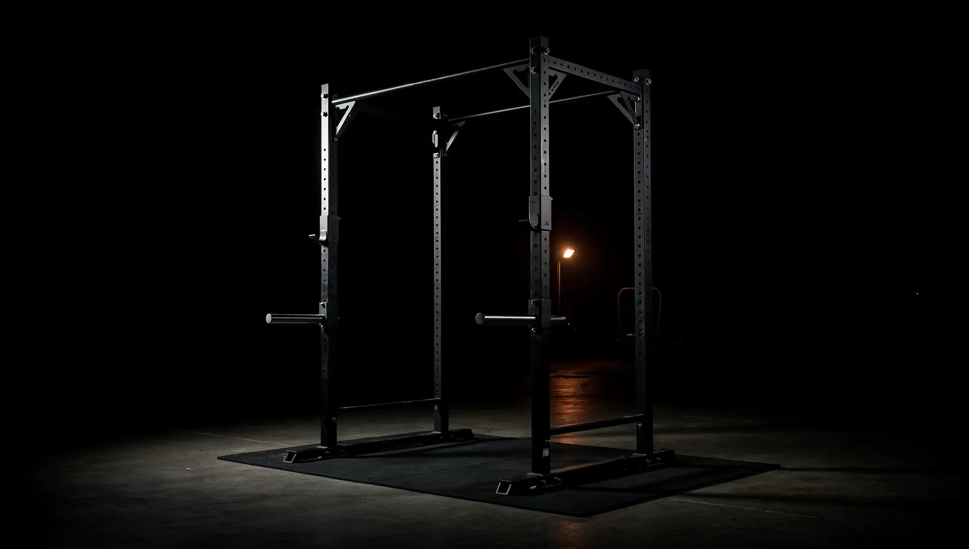 A power rack on a platform in an otherwise empty dark room, one warm light behind it.